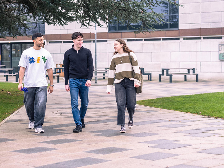 a group of three students chatting as they walk through campus